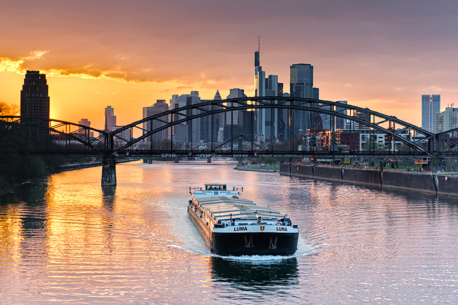 Barge passing under the Deutschherrnbrücke at sunset, Frankfurt am Main, Germany.